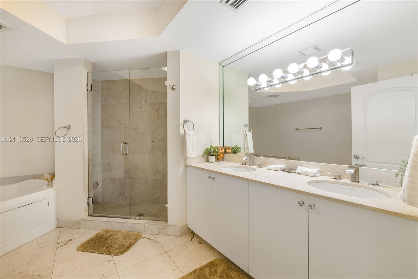 Double vanity with integrated sinks, stone-surface countertop, glass-enclosed shower featuring tile surround, oversized wall mirror, and soaking tub