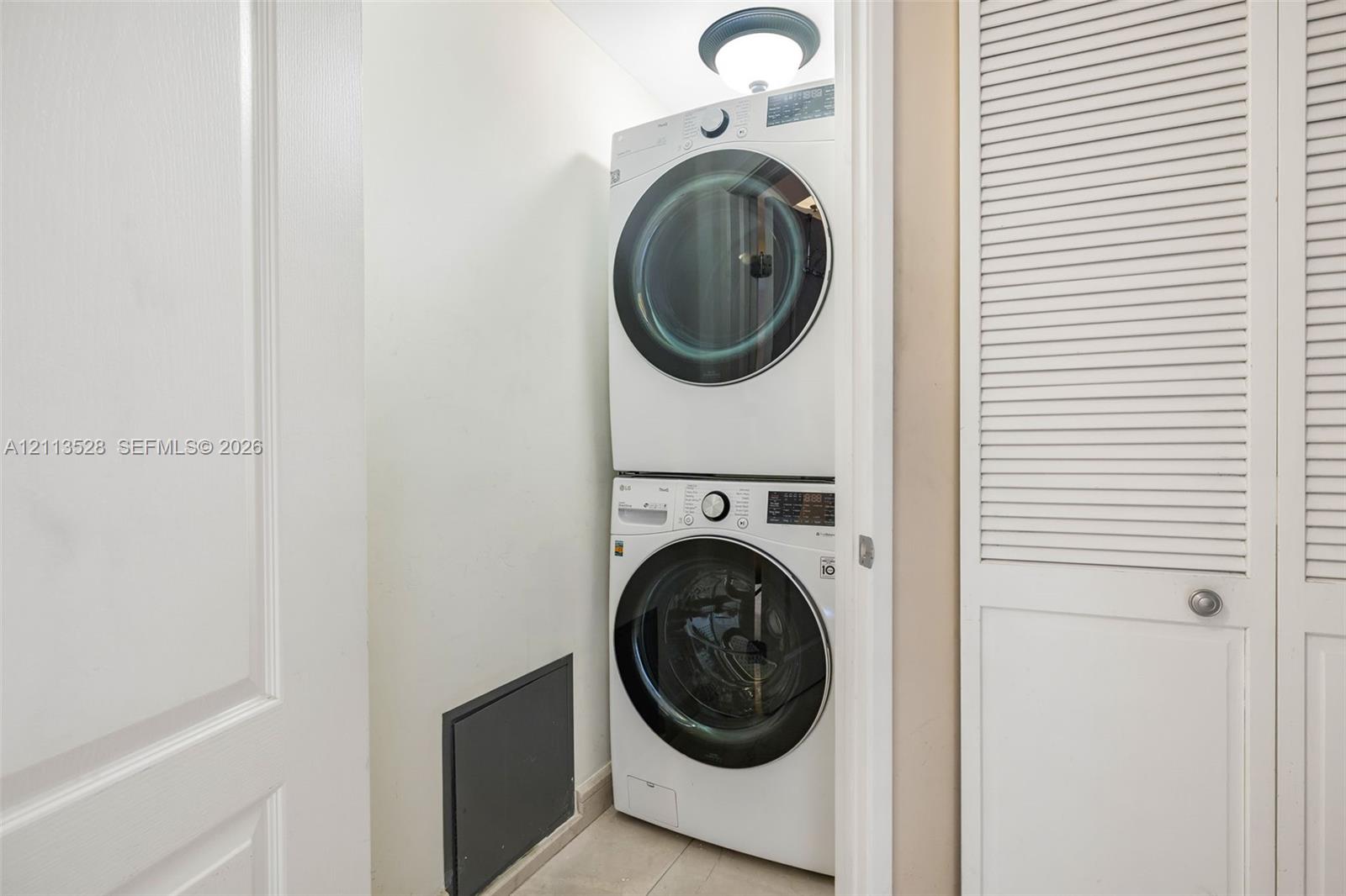 Stacked front-load laundry unit featuring a circular ceiling-mounted light fixture and white louvered closet doors