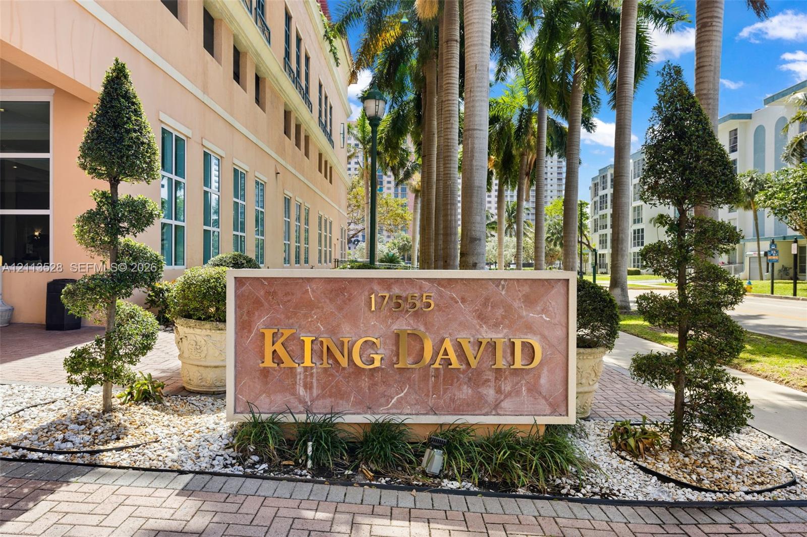 Custom stone monument sign with raised gold lettering, framed by manicured topiary trees, aggregate rock ground cover, and brick-paver landscaping