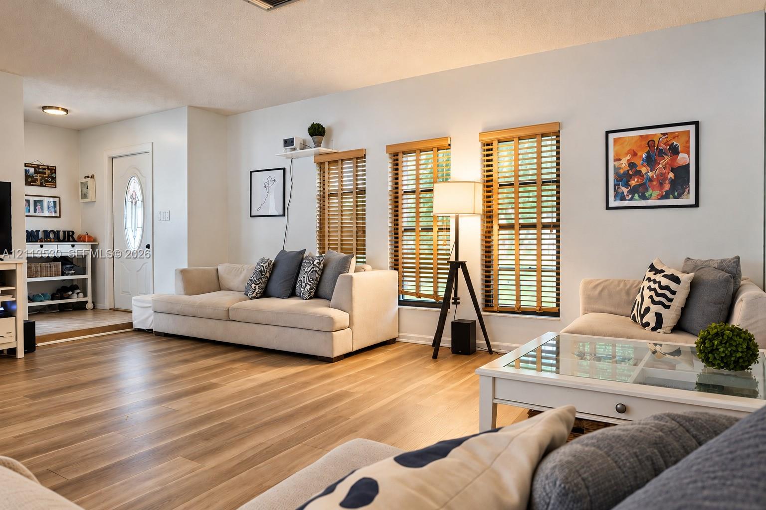 Living area featuring wood-finish flooring, white walls, and triple windows with horizontal blinds