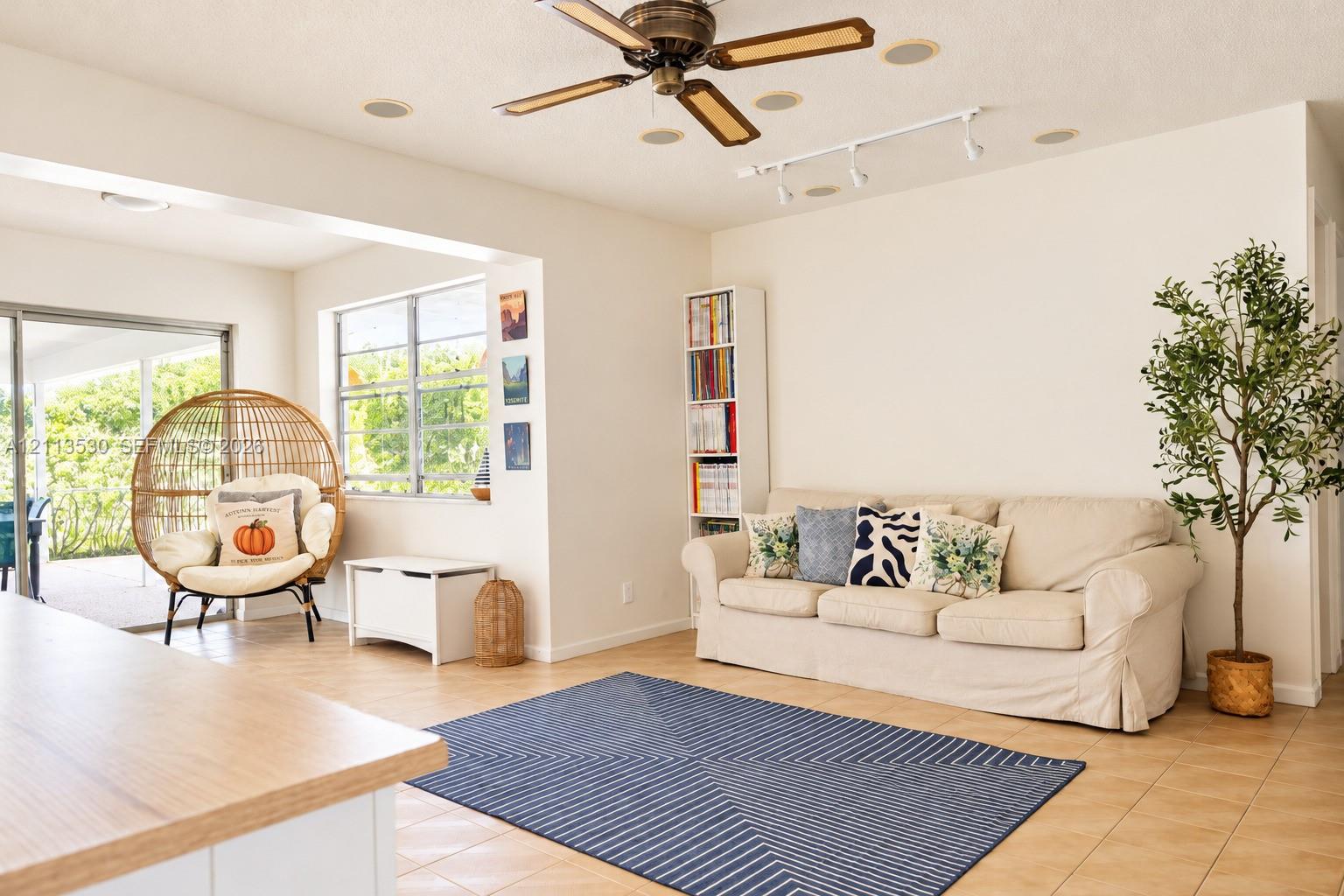 Living area featuring tile flooring, ceiling fan, track lighting, built-in shelving, and sliding glass doors