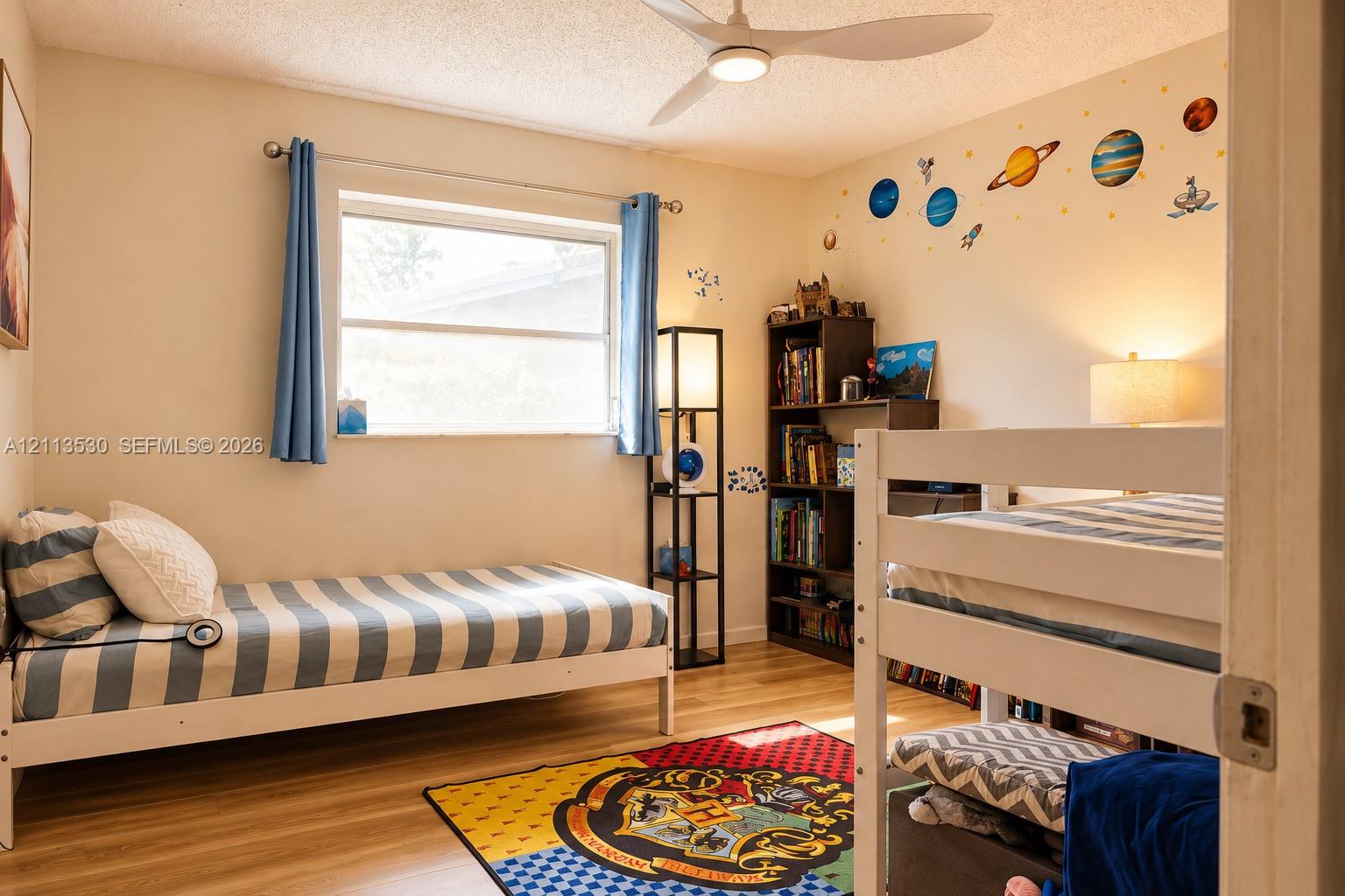 Bedroom featuring wood-finish flooring, a white three-blade ceiling fan with integrated lighting, and a large window