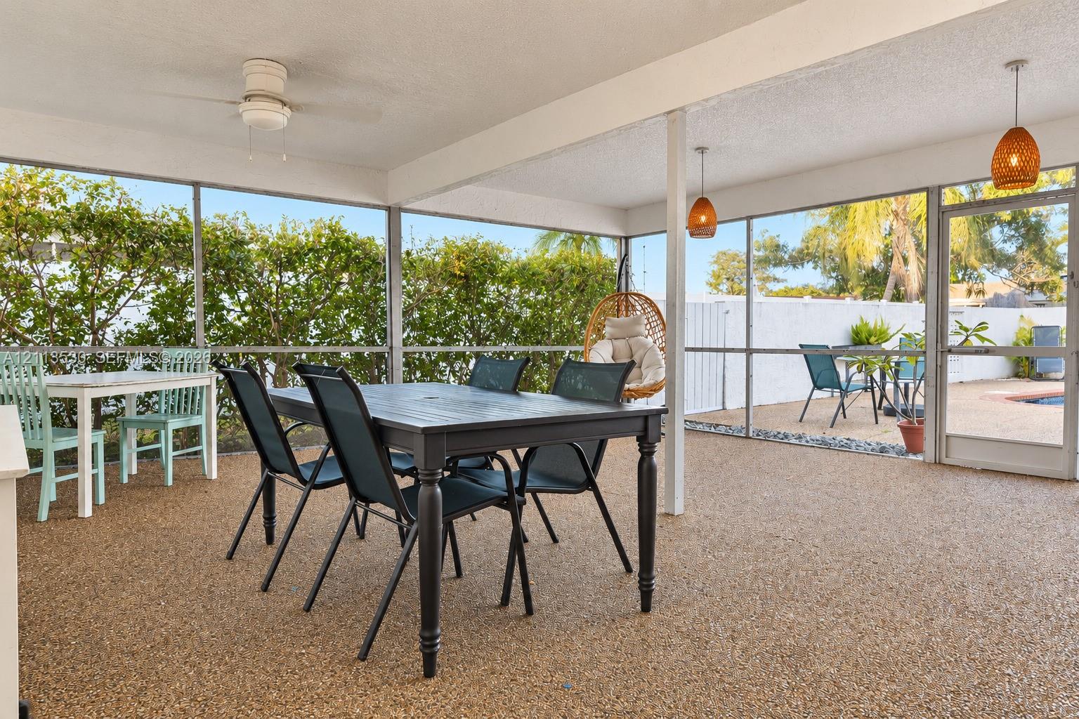 Screened-in patio featuring textured aggregate flooring, dual pendant lighting, a ceiling fan, and a glass-paneled entry door