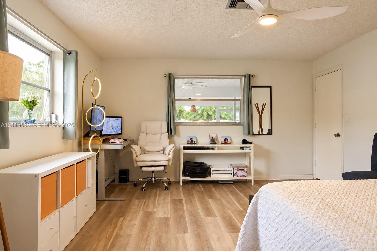 Wood-finish flooring, white walls, dual windows with natural light, and a white ceiling fan with integrated lighting