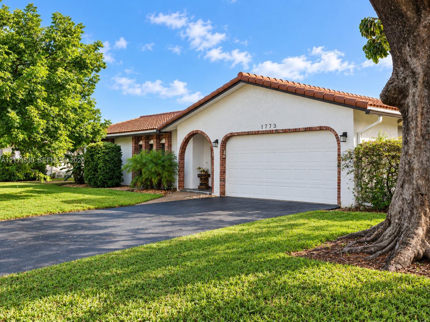 Stucco exterior residence featuring a terracotta-tiled roof, arched entryway, brick masonry detailing, and an attached multi-car garage