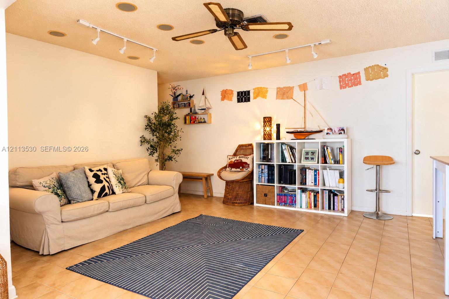 Interior space featuring neutral tile flooring, multi-directional track lighting, and a multi-blade ceiling fan