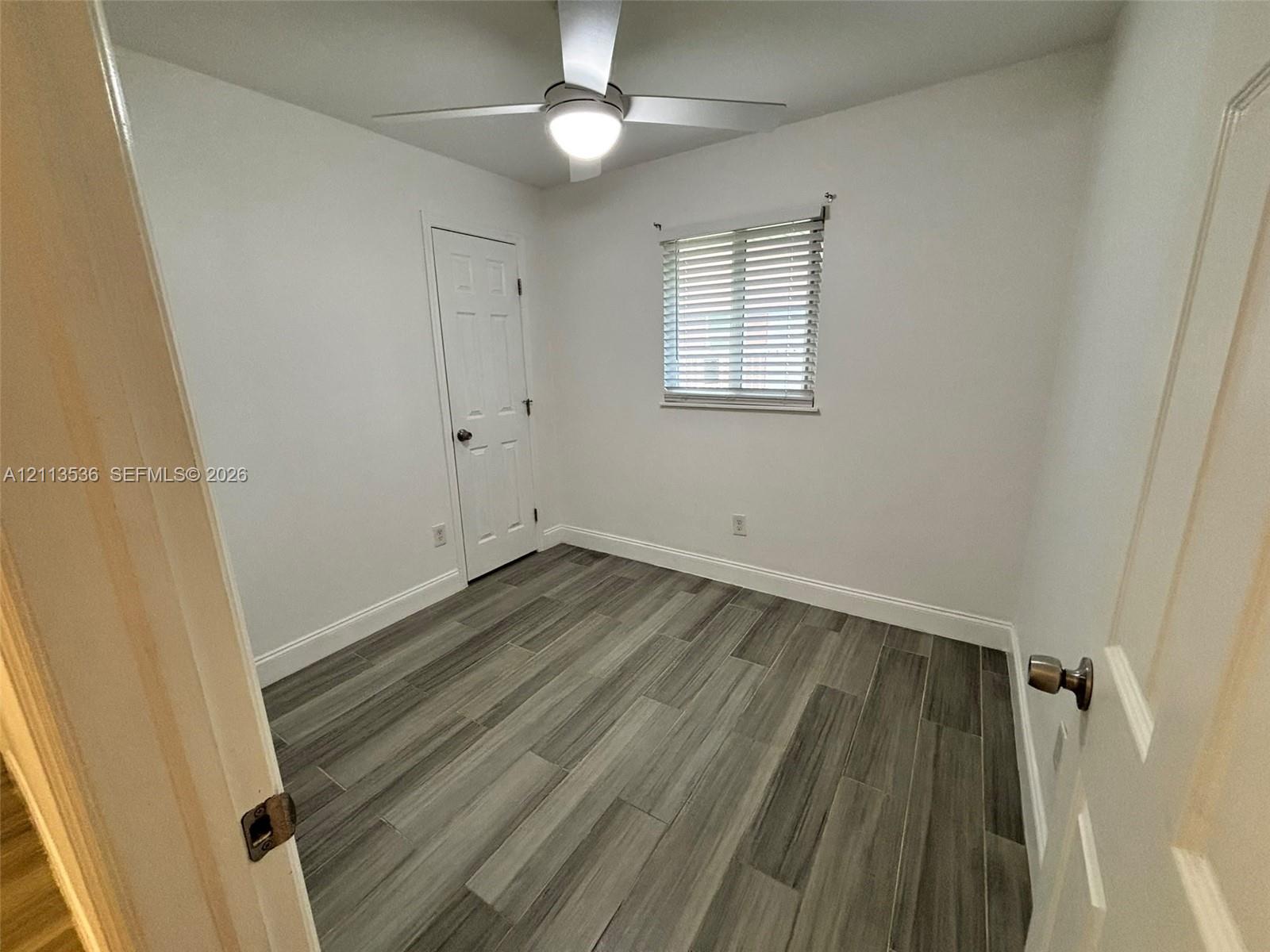 Room featuring wood-finish flooring, a ceiling-mounted light fixture with fan, and a single-panel interior door Room featuring wood-finish flooring, a ceiling-mounted light fixture with fan, and a single-panel interior door