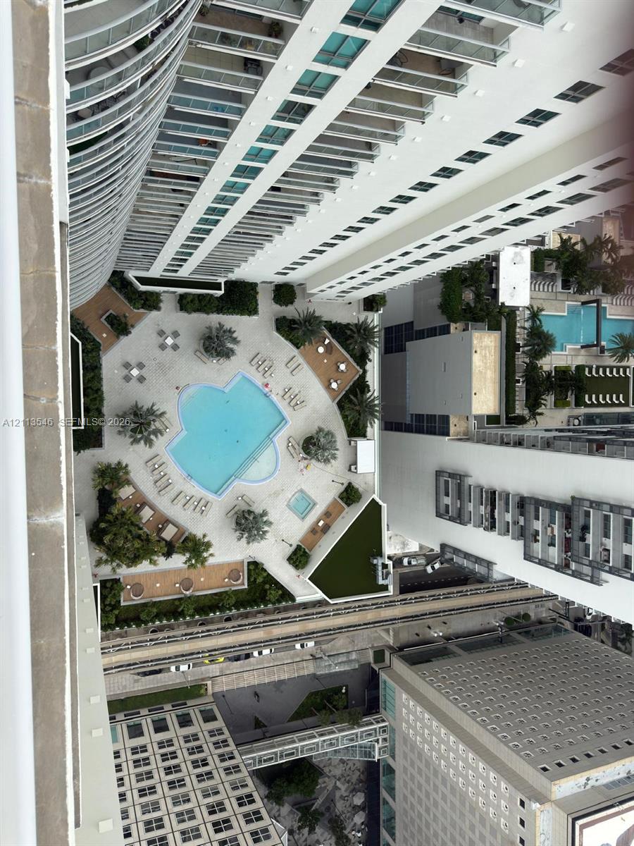 Aerial perspective of a high-rise exterior featuring a paved pool deck, custom-shaped swimming pool, built-in spa, and landscaped greenery Aerial perspective of a high-rise exterior featuring a paved pool deck, custom-shaped swimming pool, built-in spa, and landscaped greenery