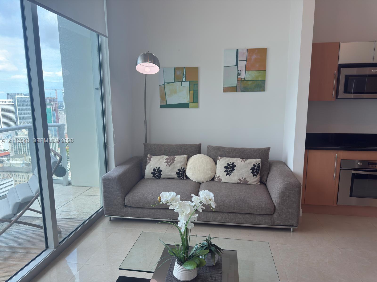 Floor-to-ceiling windows, light-toned tile flooring, and a kitchen featuring flat-panel cabinetry and stainless steel appliances Floor-to-ceiling windows, light-toned tile flooring, and a kitchen featuring flat-panel cabinetry and stainless steel appliances