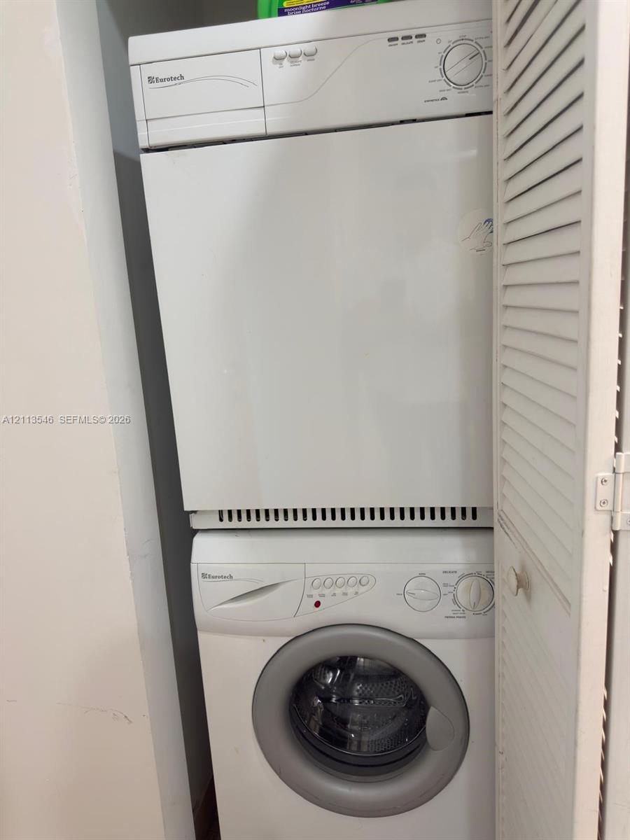Stacked laundry center featuring a front-loading washer and louvered closet doors
