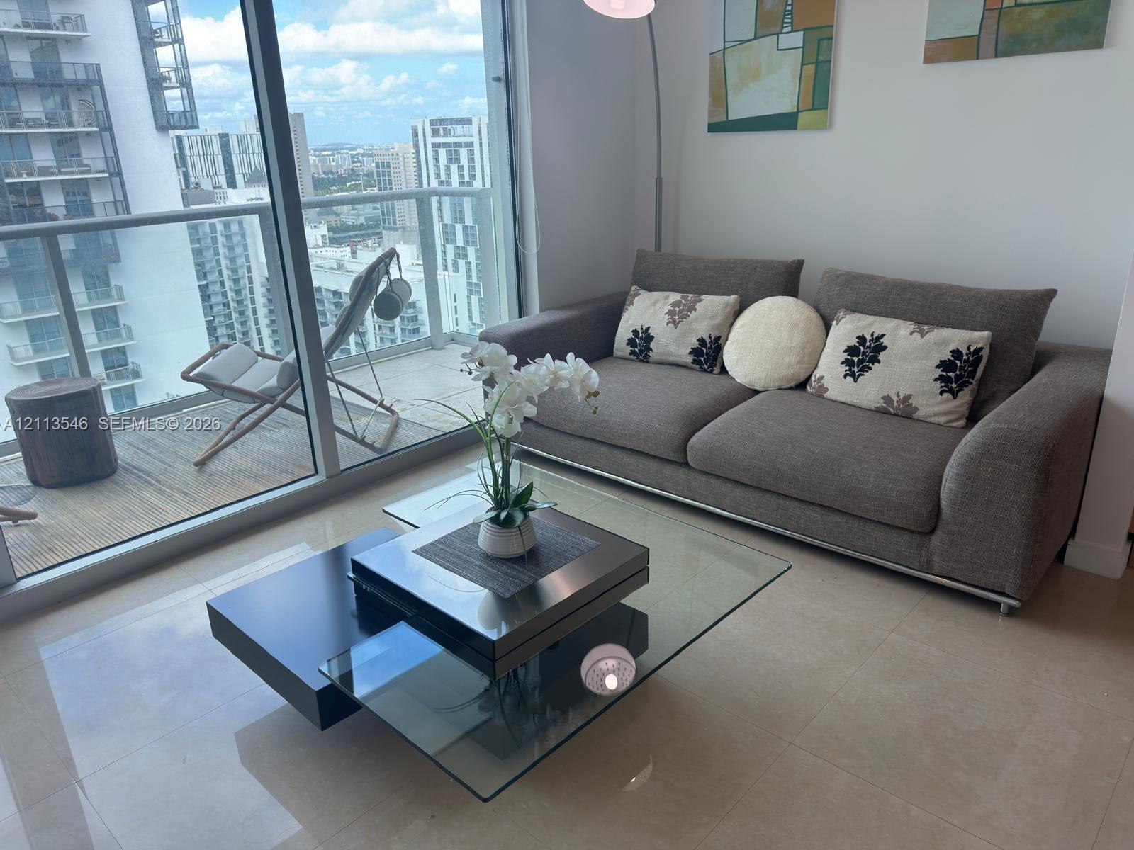 Floor-to-ceiling glass doors, neutral tile flooring, and a private balcony featuring a glass panel railing Floor-to-ceiling glass doors, neutral tile flooring, and a private balcony featuring a glass panel railing