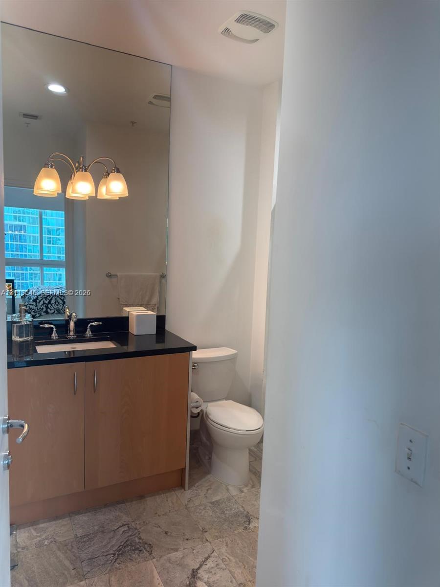 Bathroom featuring wood-finish cabinetry, a dark stone countertop with an integrated basin, a full-height wall mirror, and stone flooring