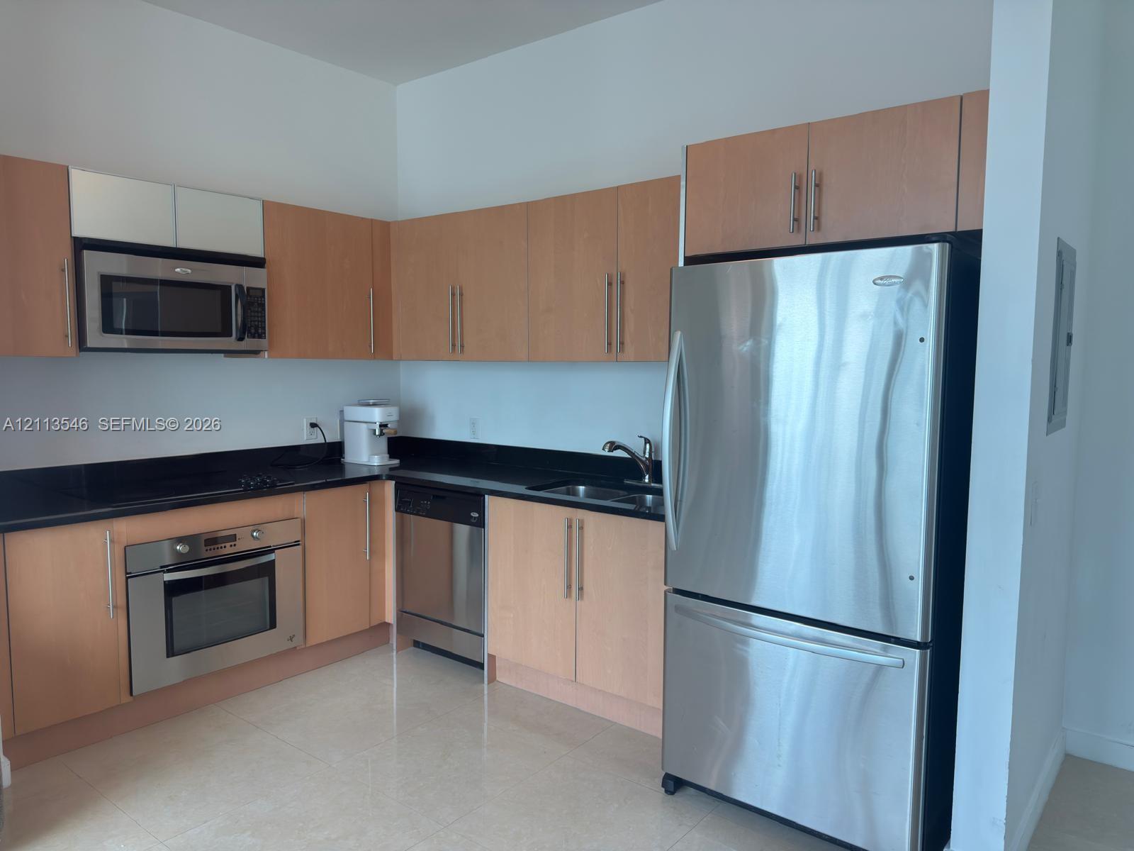 Kitchen featuring flat-panel wood-finish cabinetry, dark solid-surface countertops, stainless steel appliances, and tile flooring Kitchen featuring flat-panel wood-finish cabinetry, dark solid-surface countertops, stainless steel appliances, and tile flooring