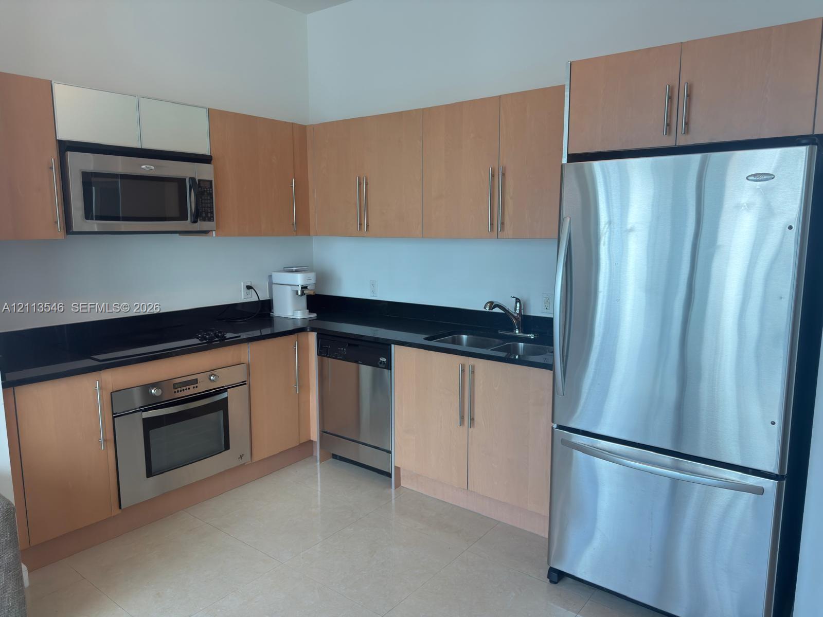 Kitchen featuring light-finish cabinetry, black countertops, stainless steel appliances, a built-in oven, and tile flooring Kitchen featuring light-finish cabinetry, black countertops, stainless steel appliances, a built-in oven, and tile flooring
