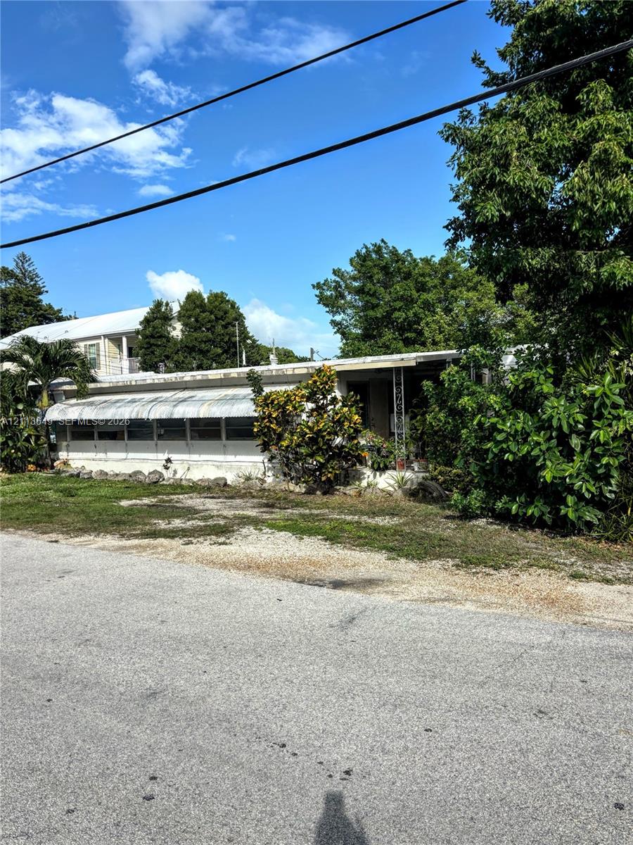 Exterior featuring a single-story structure with an attached metal awning, decorative metal porch supports, and mature perimeter landscaping