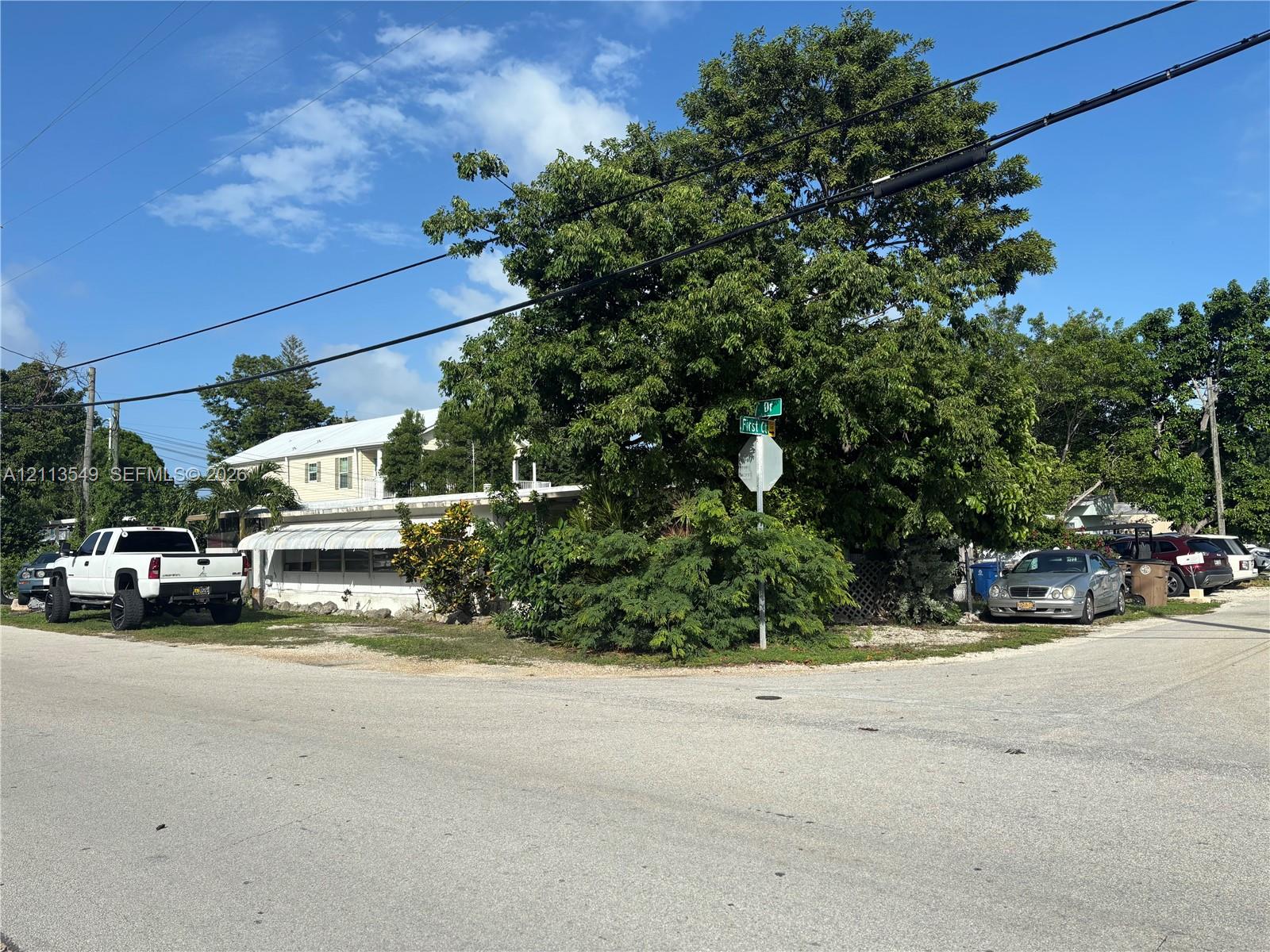 Corner lot featuring light-colored exterior siding, an expansive awning, and established mature trees