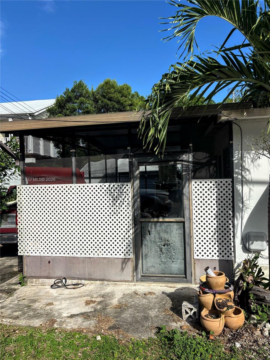 Enclosed porch featuring metal framing, diamond-pattern lattice panels, a glass-pane door, and a concrete patio foundation
