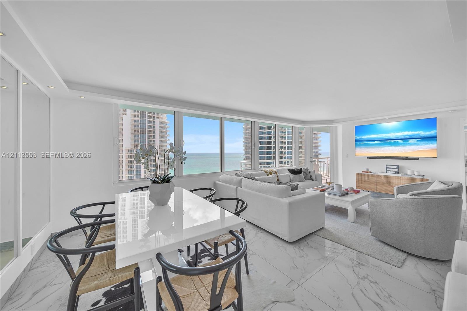 Open-concept living space featuring expansive floor-to-ceiling windows, polished stone-finish flooring, recessed lighting, and wall-mounted media cabinetry