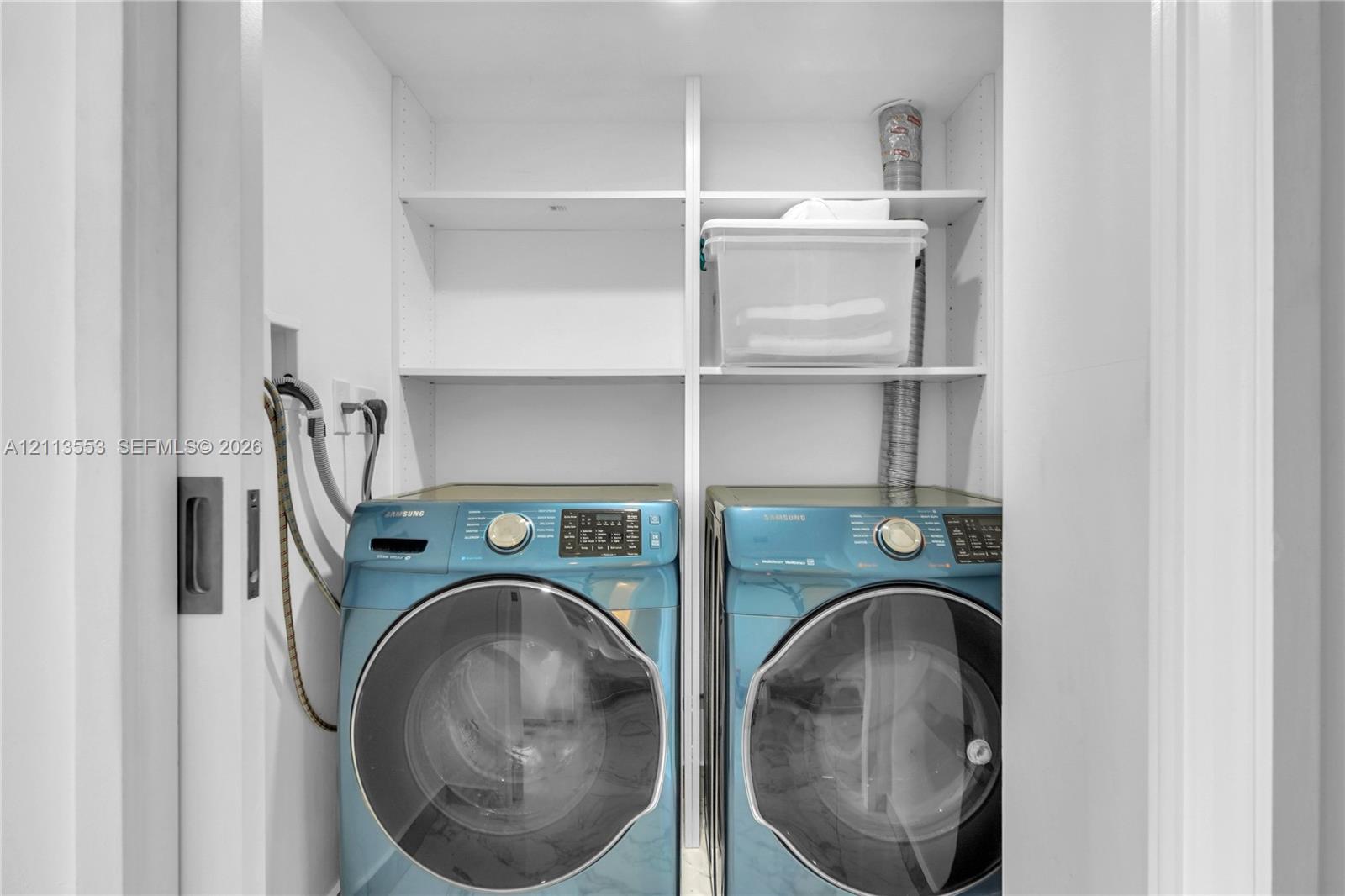 Laundry closet featuring built-in white shelving and a sliding pocket door