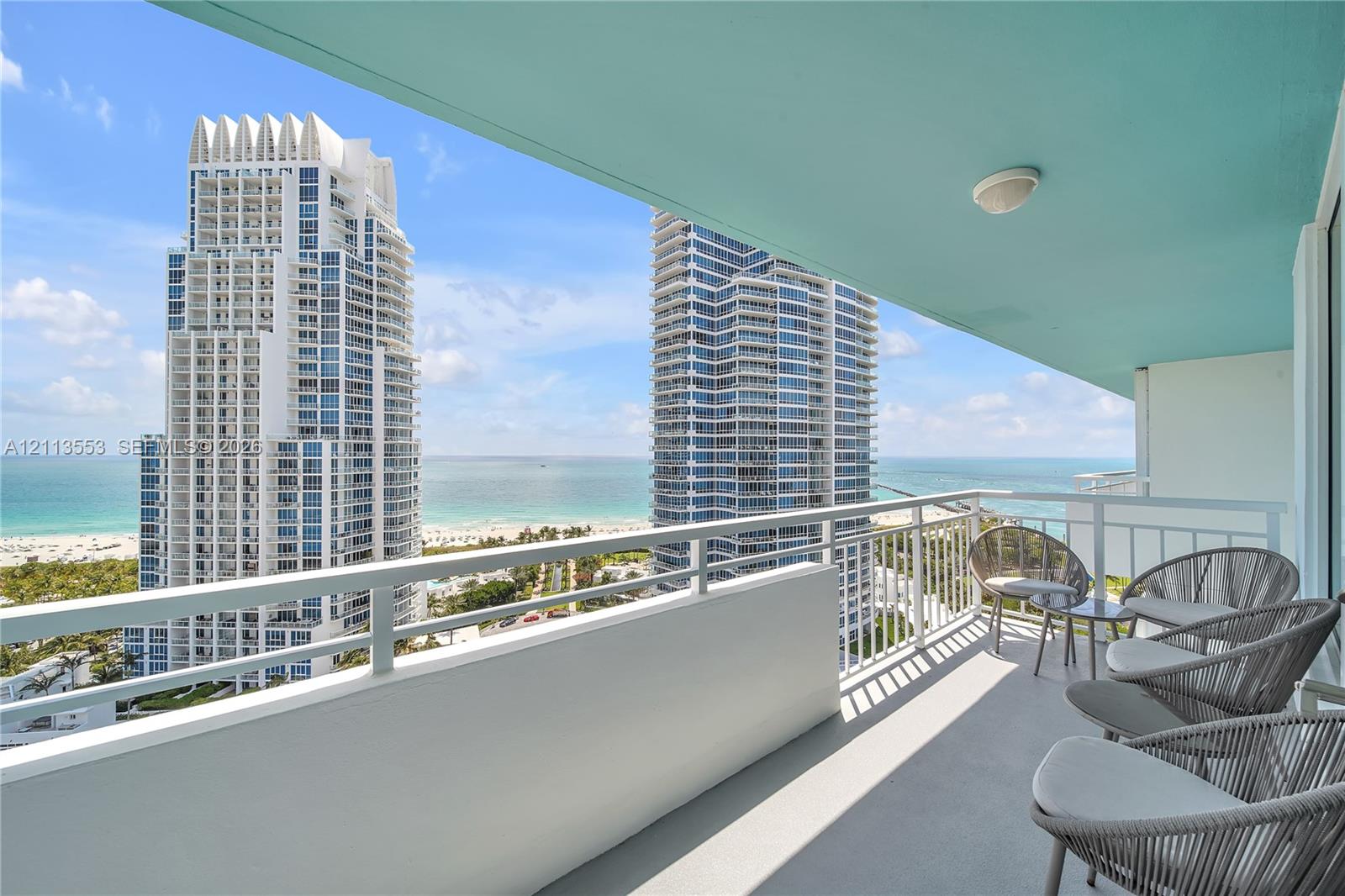 Covered balcony featuring a concrete floor, white metal railing, and ceiling-mounted lighting, showcasing a coastal horizon