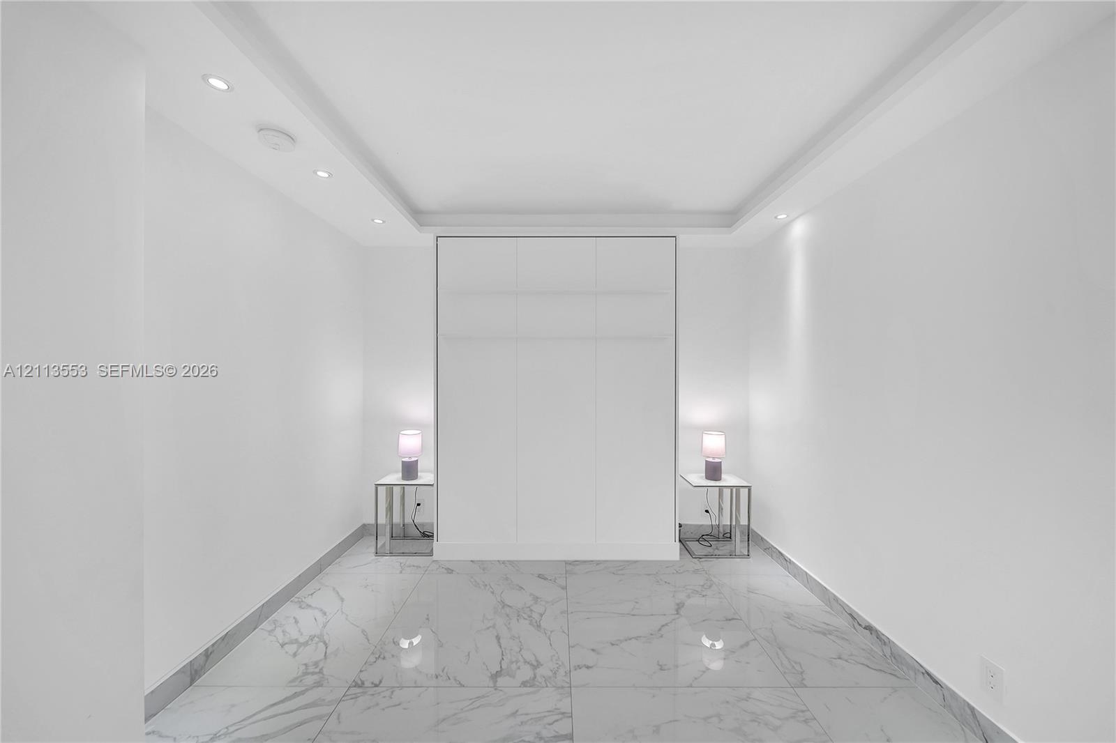 Large-format stone-look flooring, recessed ceiling lighting, tray ceiling architecture, and floor-to-ceiling built-in cabinetry