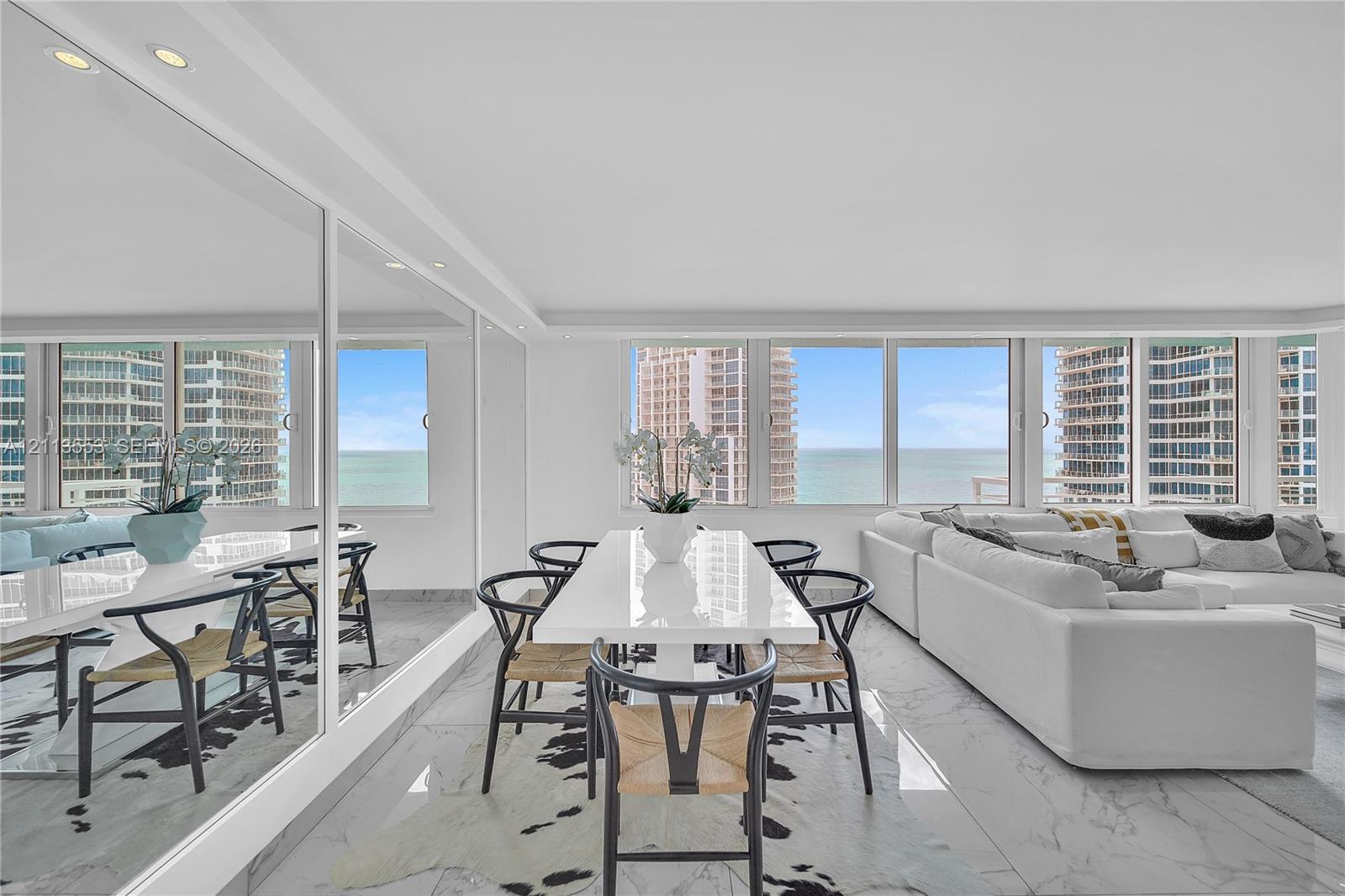 Open-concept living space featuring floor-to-ceiling windows, polished stone flooring, and expansive wall-mounted mirrors with integrated recessed lighting Open-concept living space featuring floor-to-ceiling windows, polished stone flooring, and expansive wall-mounted mirrors with integrated recessed lighting