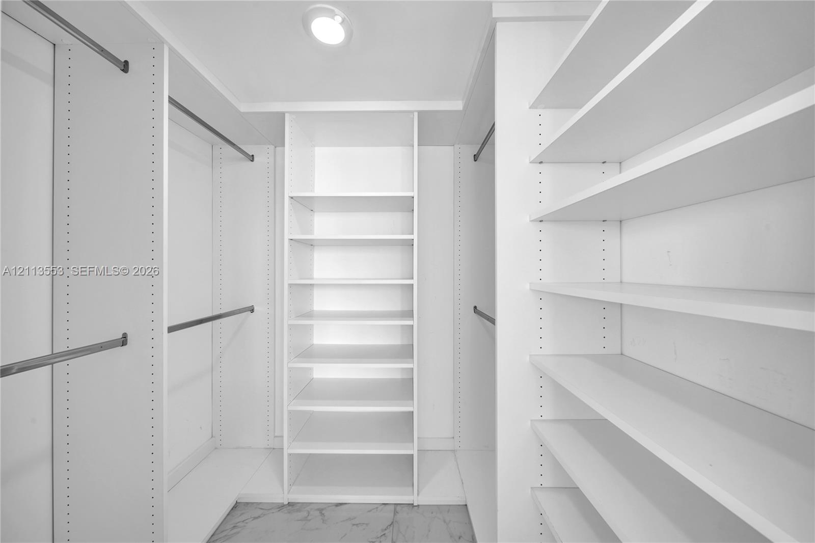 Custom walk-in closet featuring white built-in shelving, adjustable storage racks, metal garment rods, and stone-finish flooring