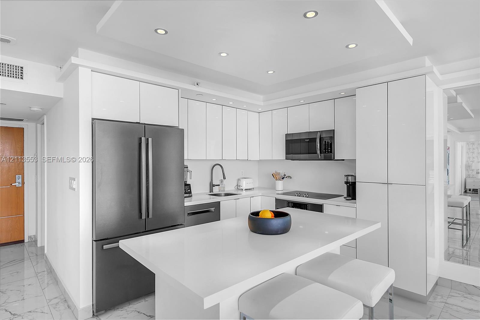 Kitchen featuring high-gloss white cabinetry, white stone countertops, an oversized center island, stainless steel appliances, and recessed ceiling lighting