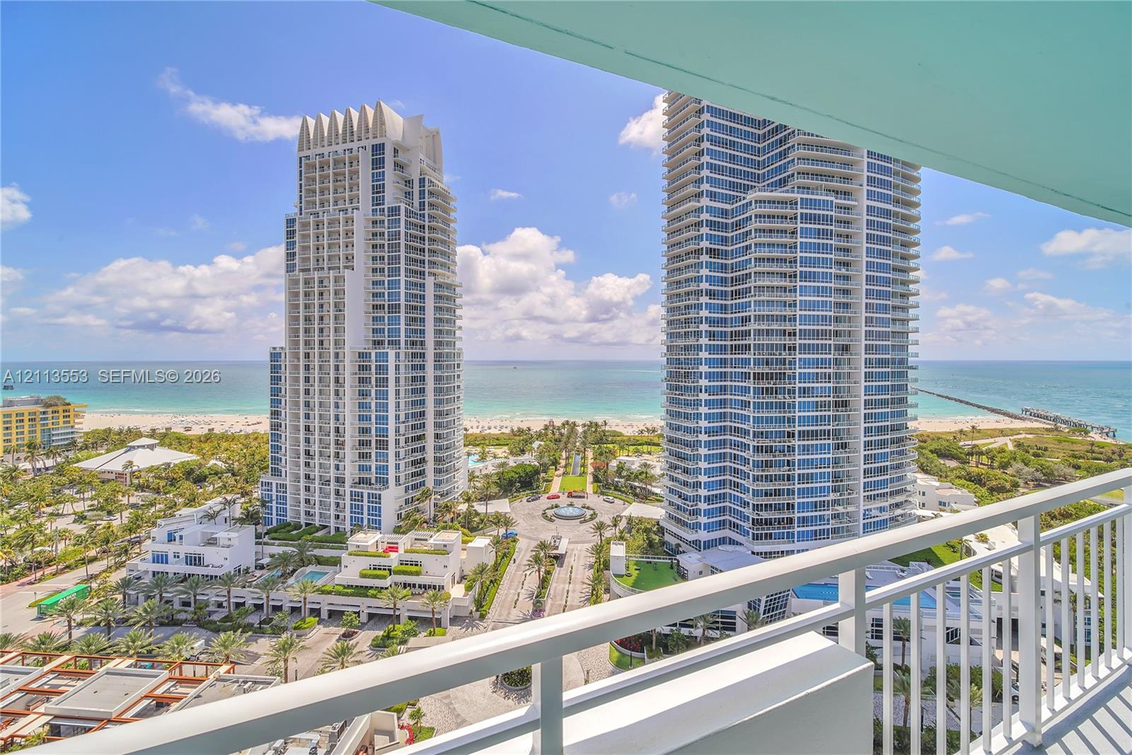 Covered balcony with white metal railings, overlooking coastal high-rise towers, sandy beach, and ocean horizon