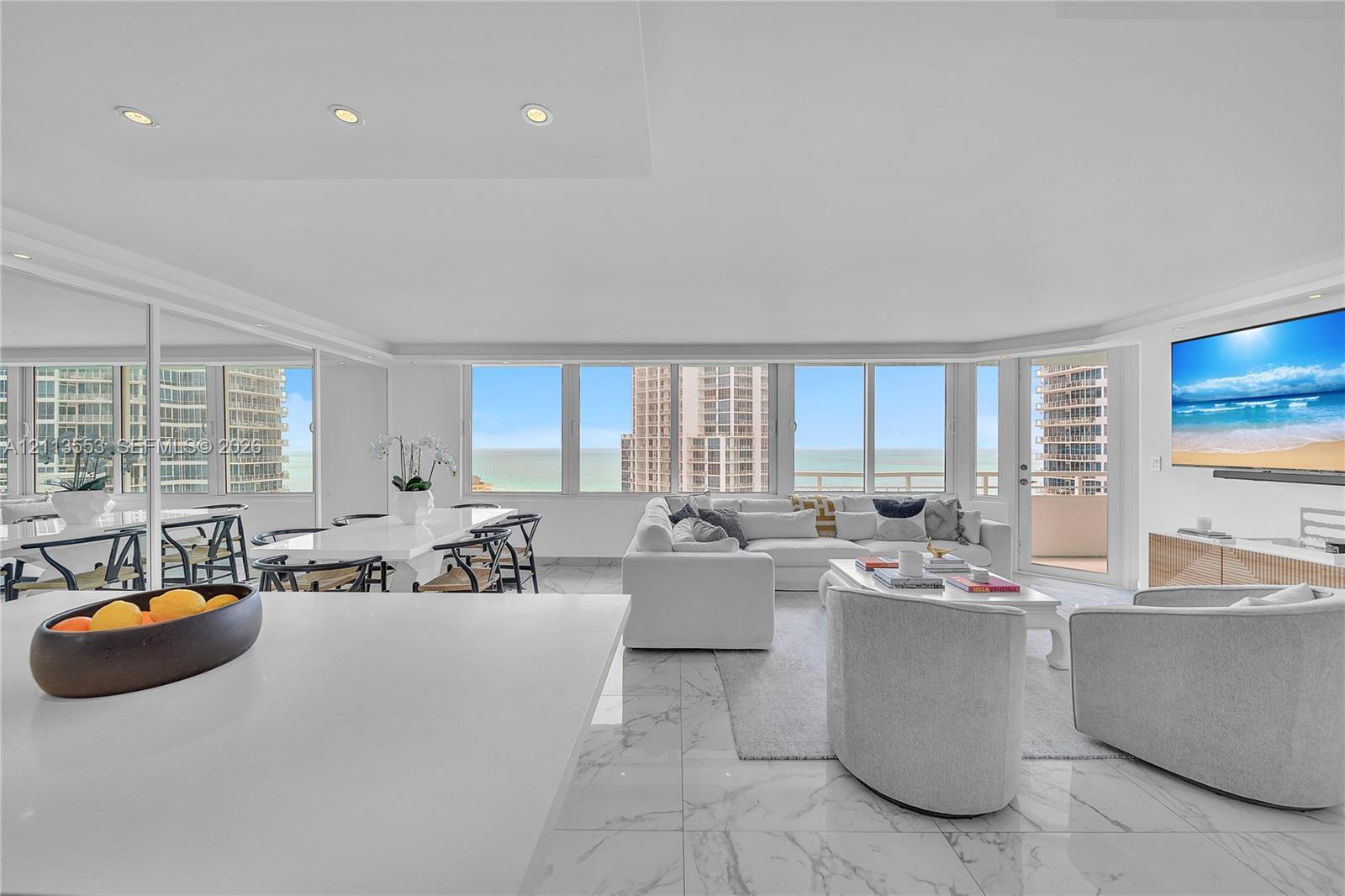 Open-concept living area featuring floor-to-ceiling windows, polished stone flooring, recessed lighting, and a private balcony