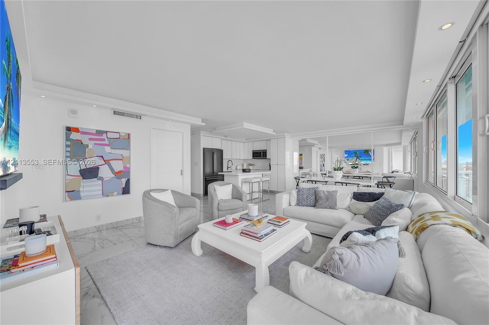 Open-concept interior featuring light-toned stone flooring, recessed ceiling lighting, a kitchen island with stone countertops, and floor-to-ceiling windows Open-concept interior featuring light-toned stone flooring, recessed ceiling lighting, a kitchen island with stone countertops, and floor-to-ceiling windows