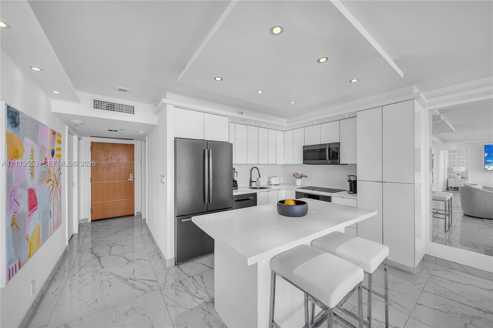 Modern kitchen featuring flat-panel white cabinetry, a center island with a quartz countertop, recessed ceiling lighting, and tile flooring with a stone-finish pattern Modern kitchen featuring flat-panel white cabinetry, a center island with a quartz countertop, recessed ceiling lighting, and tile flooring with a stone-finish pattern