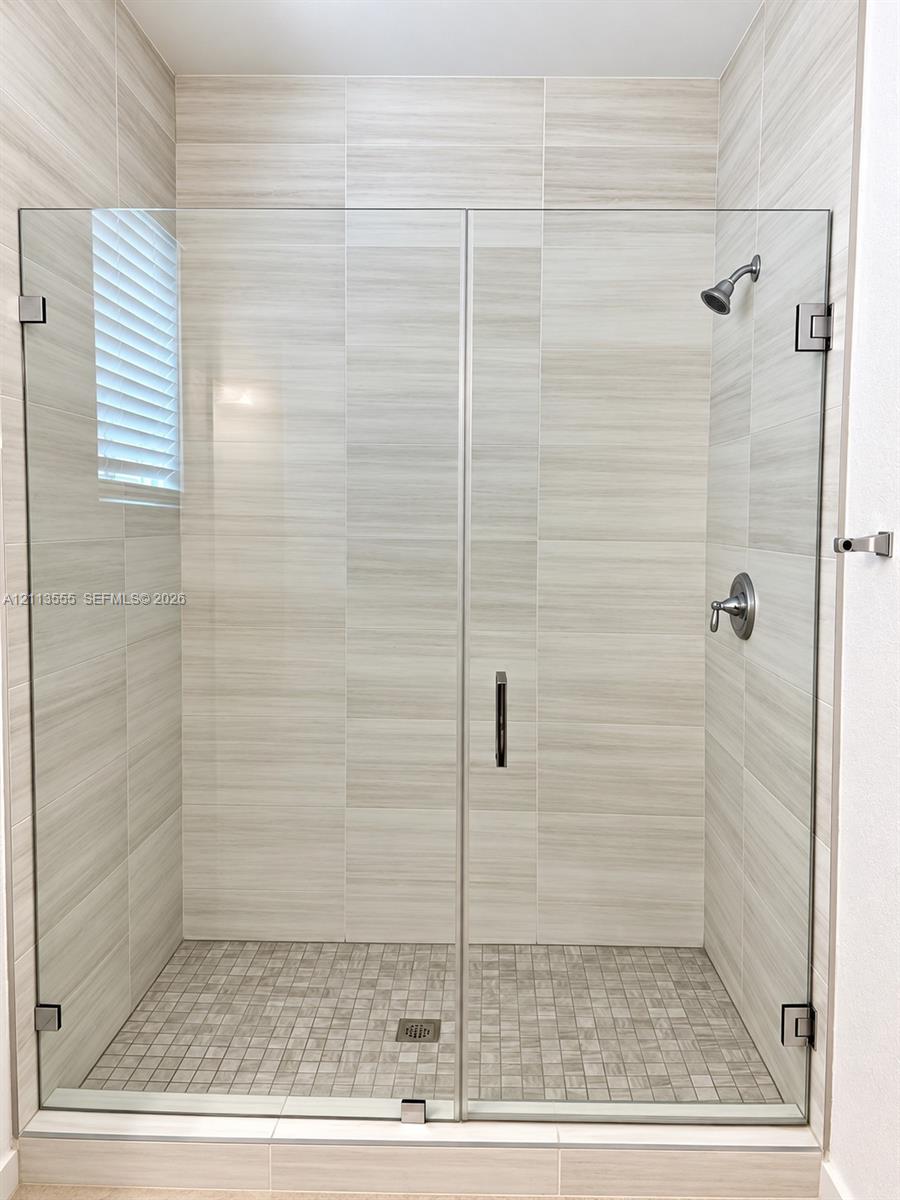 Walk-in shower featuring a frameless glass door, floor-to-ceiling large-format neutral tile, mosaic tile flooring, and wall-mounted metal fixtures
