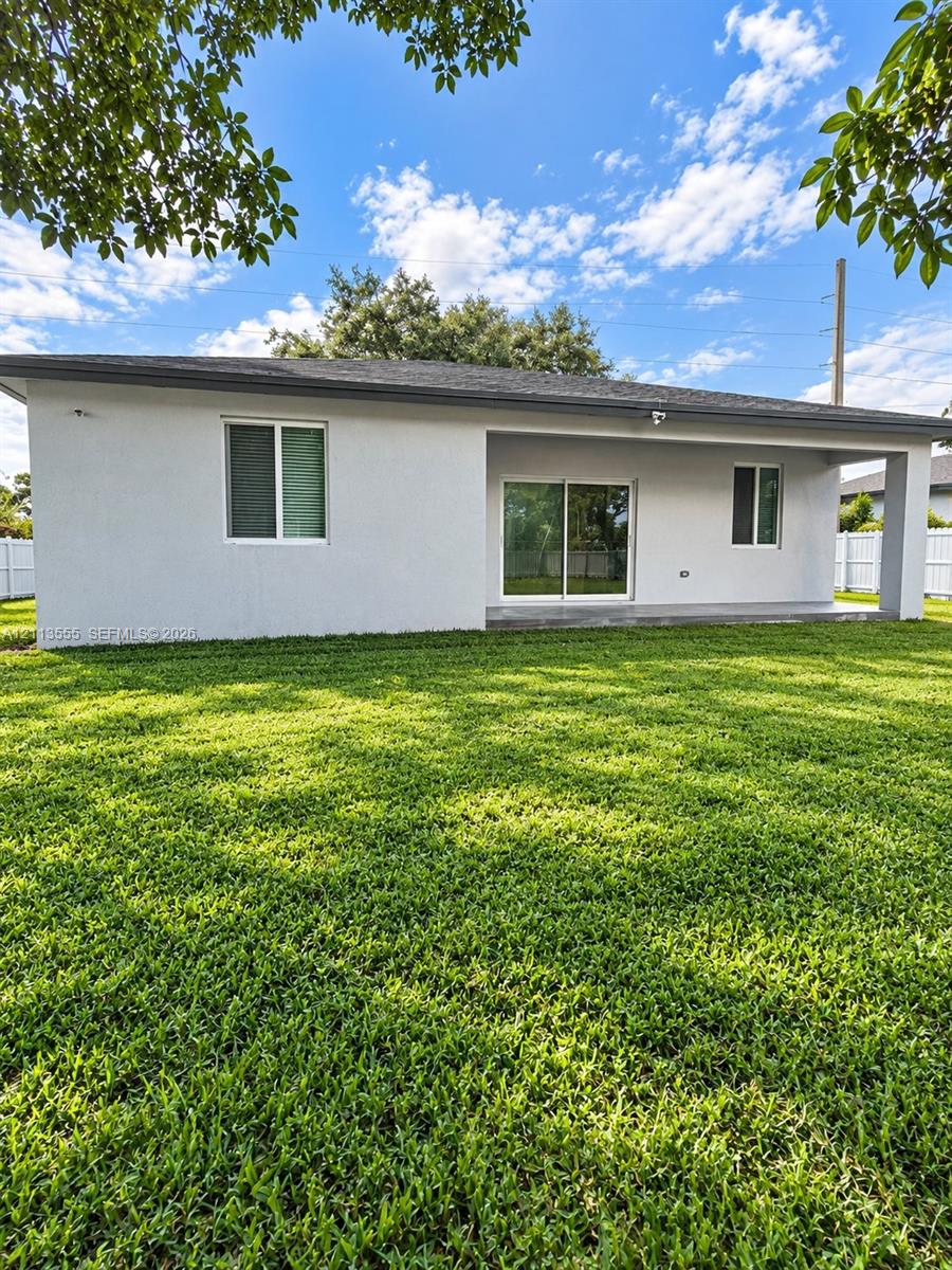 Rear exterior featuring a covered concrete patio, sliding glass doors, white vinyl perimeter fencing, and a manicured lawn Rear exterior featuring a covered concrete patio, sliding glass doors, white vinyl perimeter fencing, and a manicured lawn