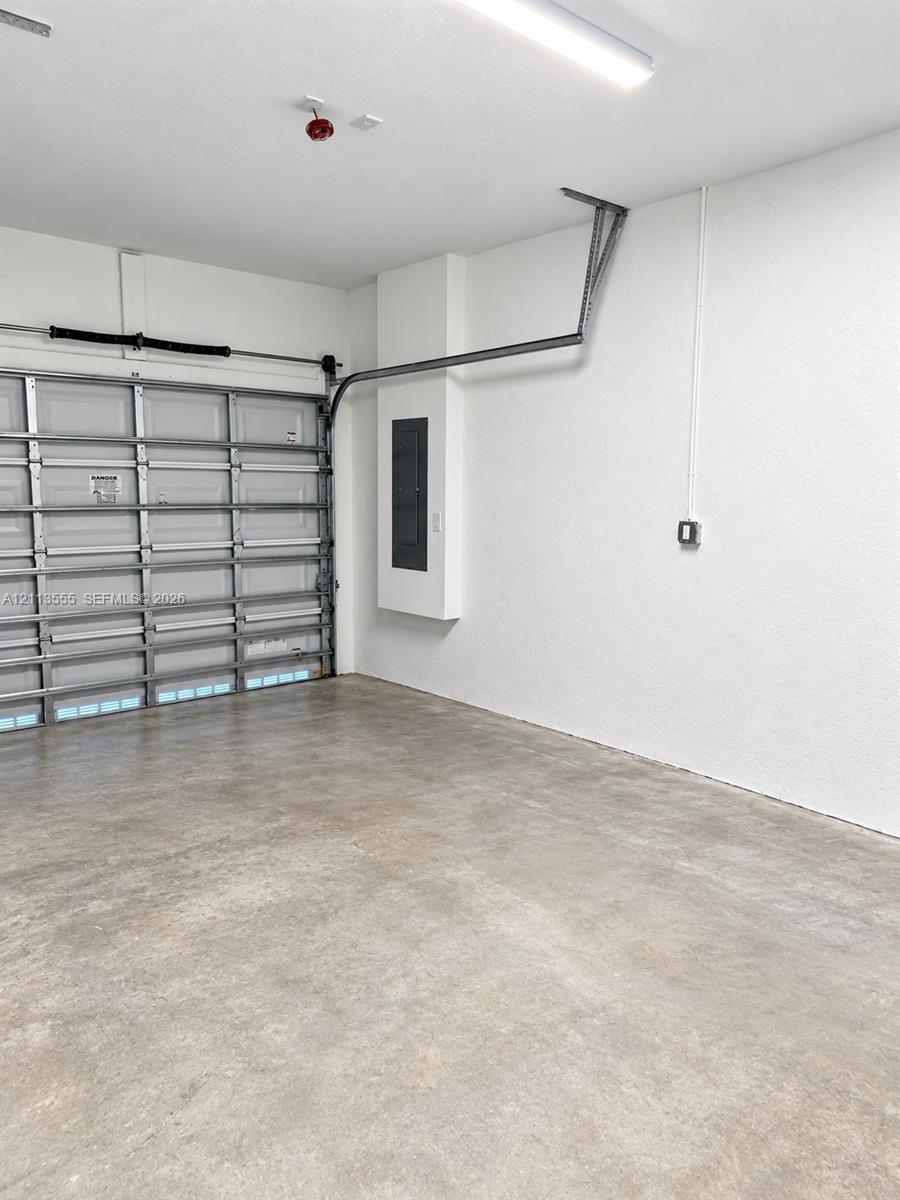 Garage interior featuring a concrete floor, sectional overhead door, linear LED lighting, and a recessed electrical service panel