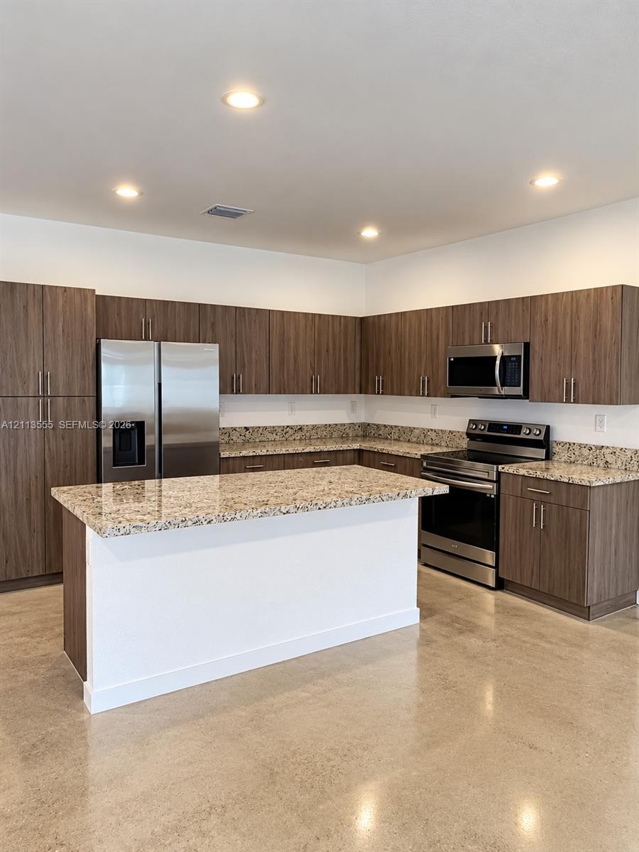 Kitchen featuring flat-panel wood-finish cabinetry, stone-surface countertops, a center island, polished concrete flooring, and stainless steel appliances