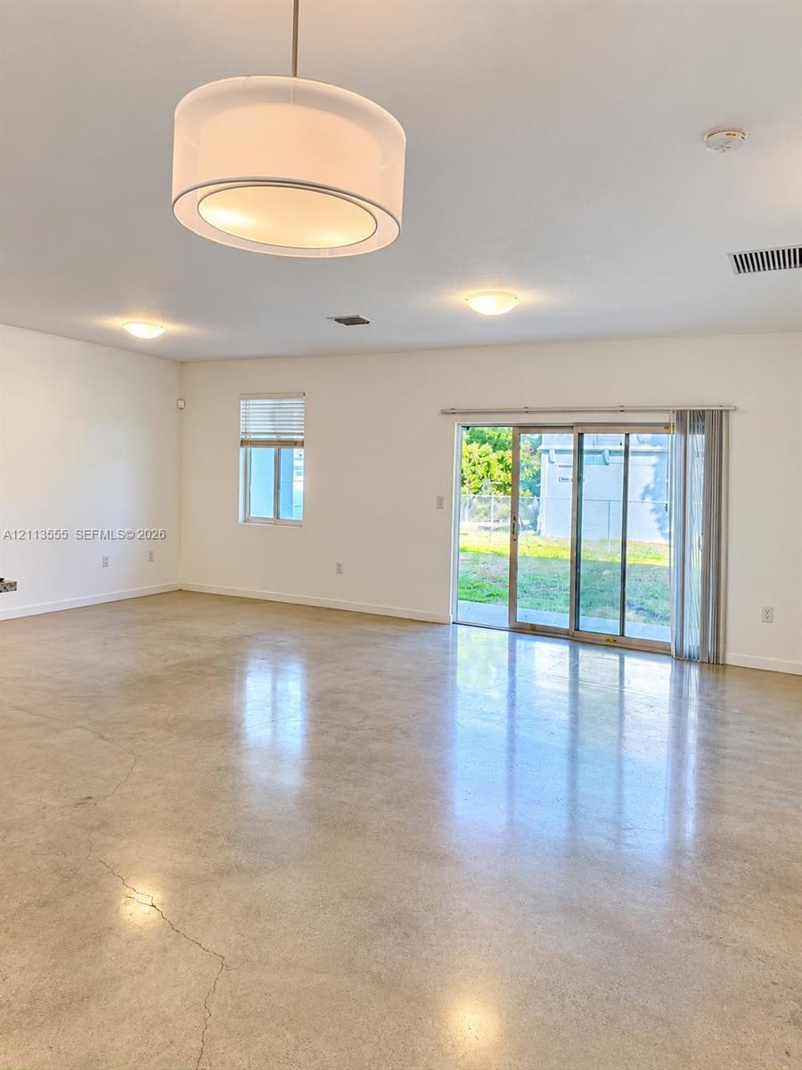 Polished concrete flooring, drum-style pendant lighting, recessed ceiling lights, and a sliding glass door providing access to the exterior Polished concrete flooring, drum-style pendant lighting, recessed ceiling lights, and a sliding glass door providing access to the exterior