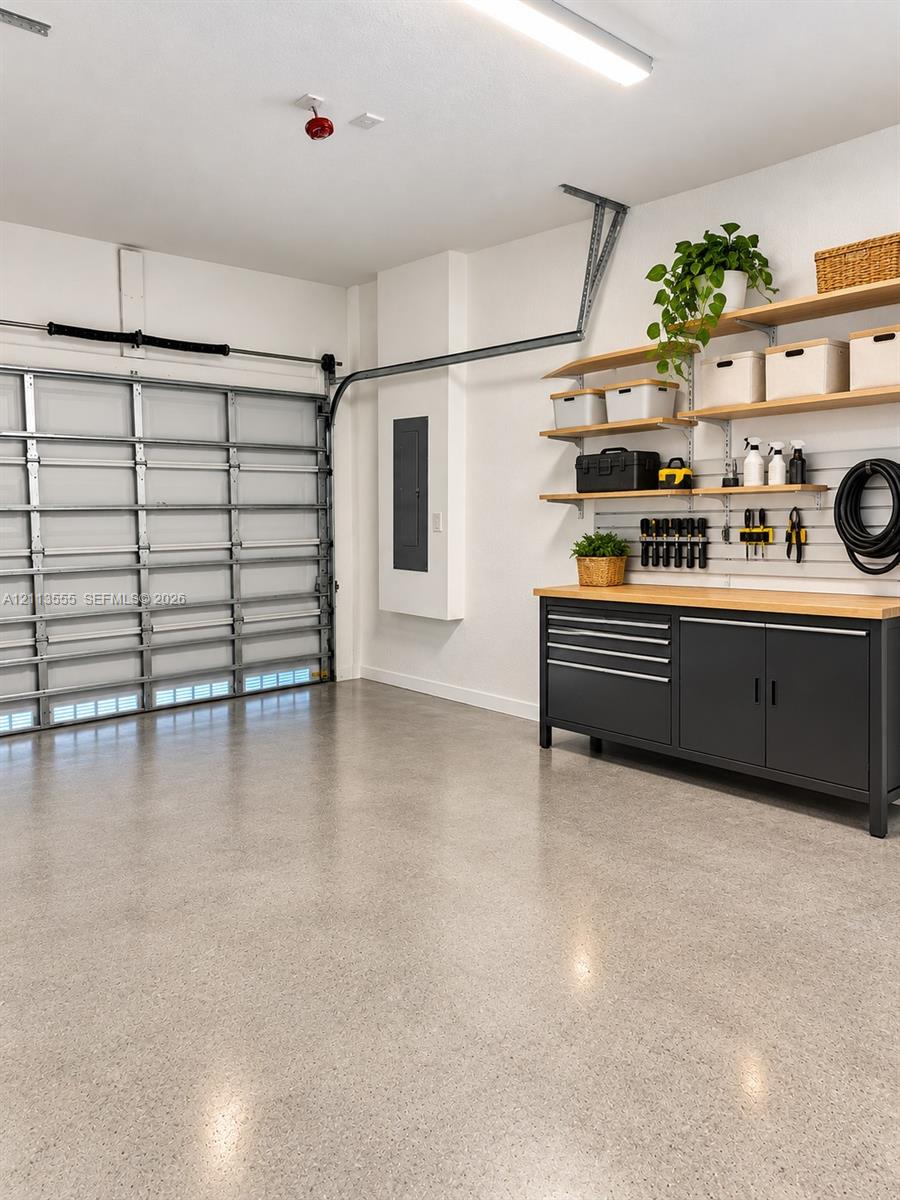 Finished garage featuring epoxy-coated flooring, built-in metal cabinetry with wood-finish work surface, wall-mounted organizational slat wall, and tiered wooden shelving