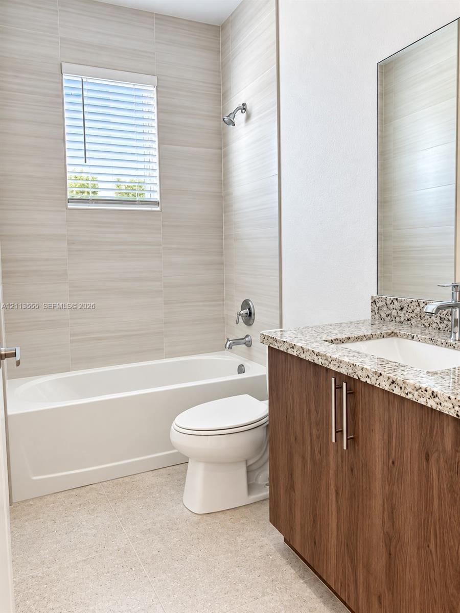 Bathroom featuring a tub-shower combination with horizontal tile surround, a wood-finish vanity with a stone-composite countertop, and a built-in recessed mirror