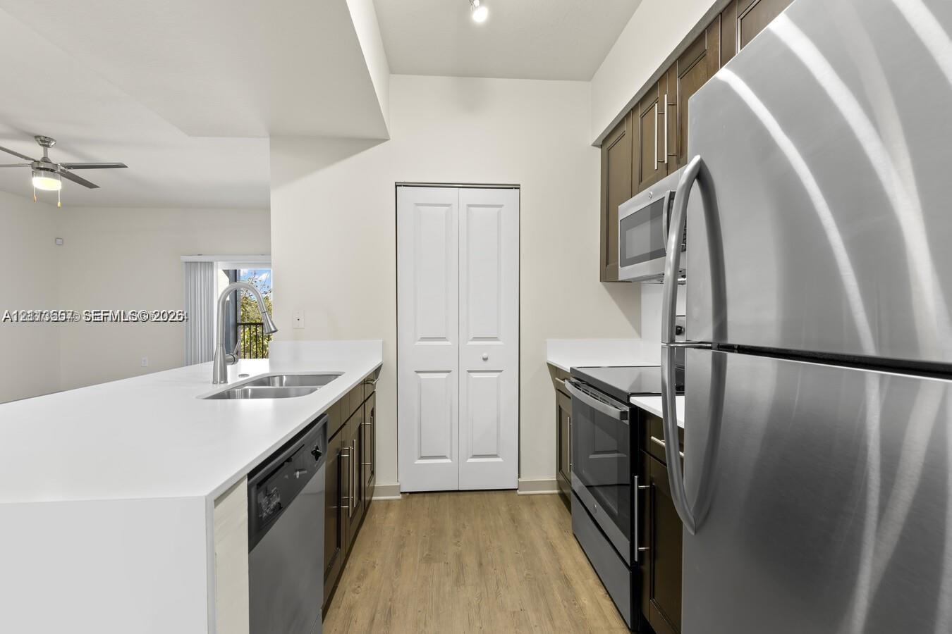 Kitchen featuring dark wood-finish cabinetry, solid-surface countertops, stainless steel appliances, a double-basin undermount sink with a pull-down faucet, and wood-finish flooring