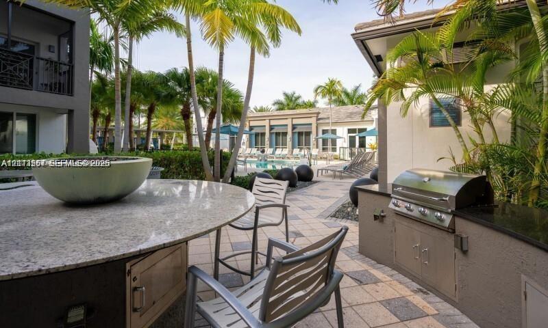 Outdoor kitchen area featuring a built-in stainless steel grill, stone-finish countertops, tile patio flooring, and a circular stone-topped bar with a central basin