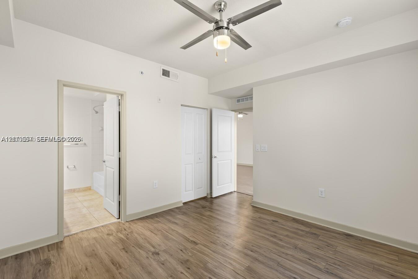 Room featuring wood-finish flooring, a ceiling fan with integrated lighting, and multiple interior doors