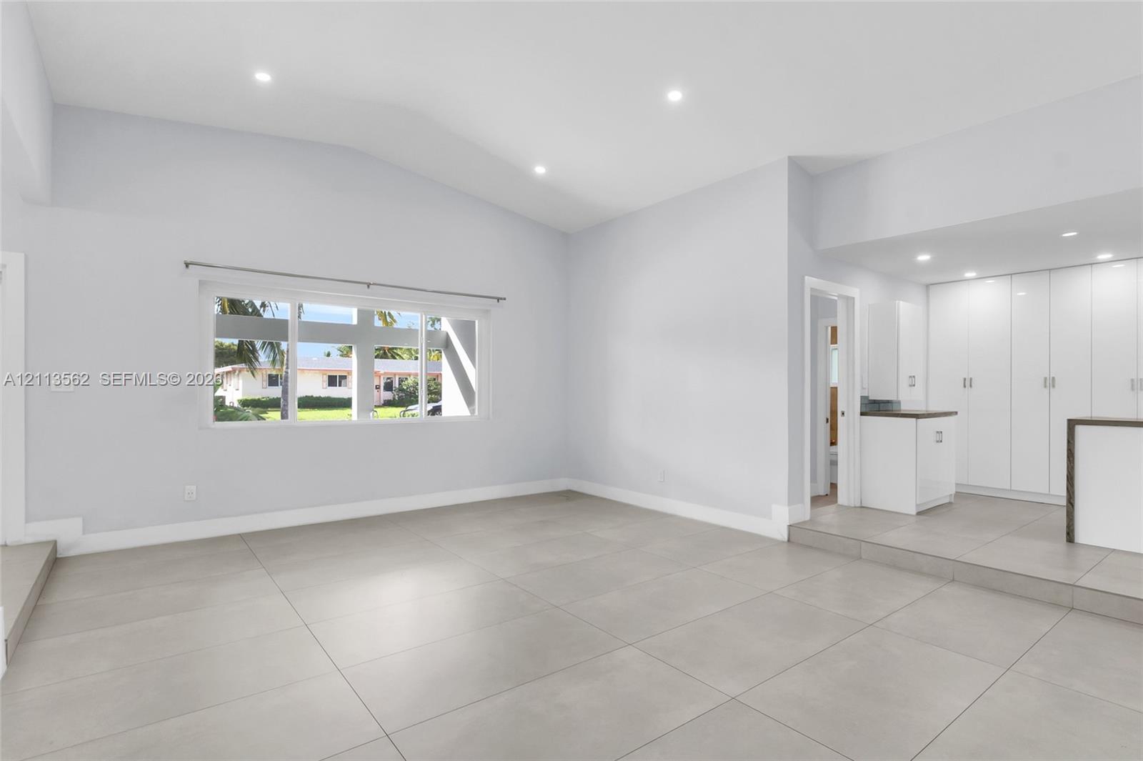 Open-concept space featuring vaulted ceilings, large-format tile flooring, recessed lighting, and built-in white cabinetry with a dedicated countertop surface