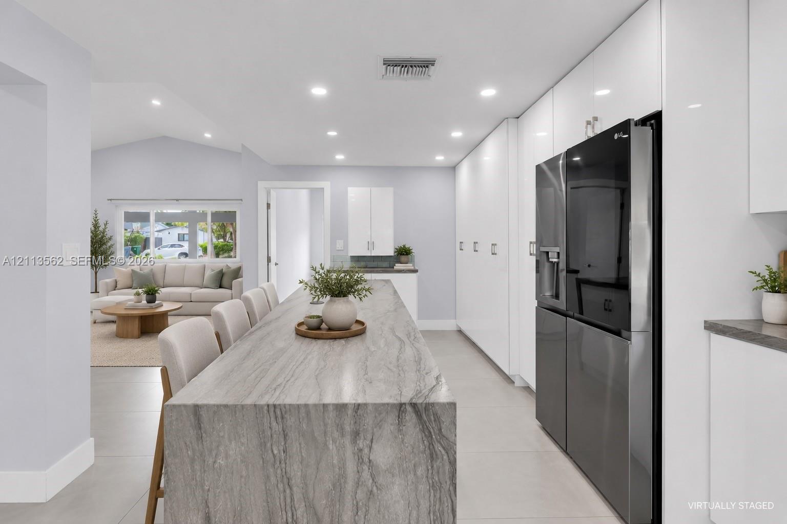 Kitchen featuring a waterfall-edge island with natural stone-patterned surfacing, floor-to-ceiling cabinetry, recessed lighting, and large-format tile flooring