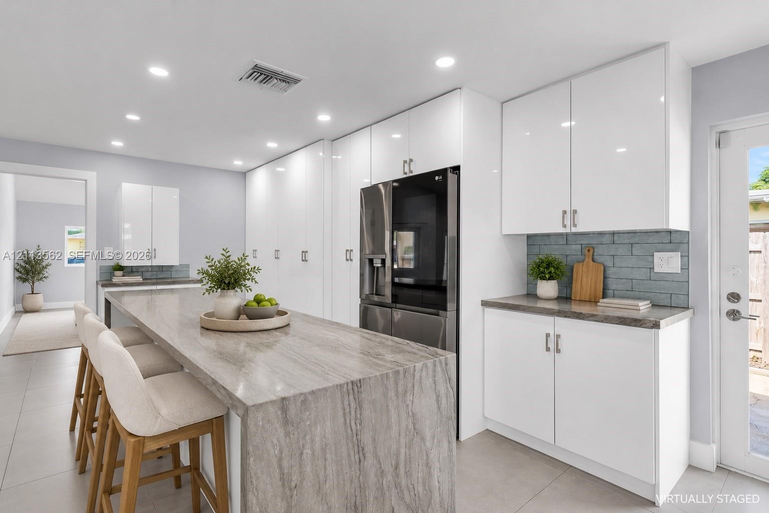 Kitchen featuring high-gloss white cabinetry, waterfall-edge stone island, gray subway tile backsplash, and recessed lighting