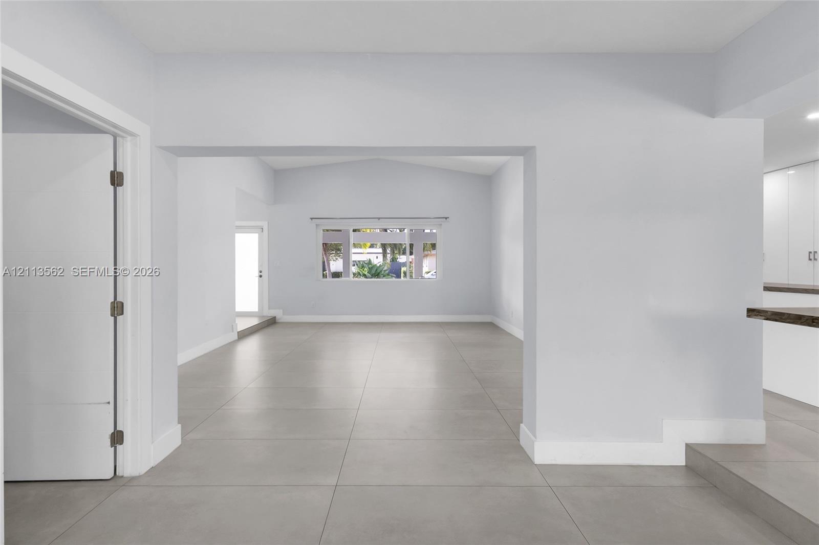 Large-format tile flooring, vaulted ceiling, wide interior entryway, and oversized multi-pane window