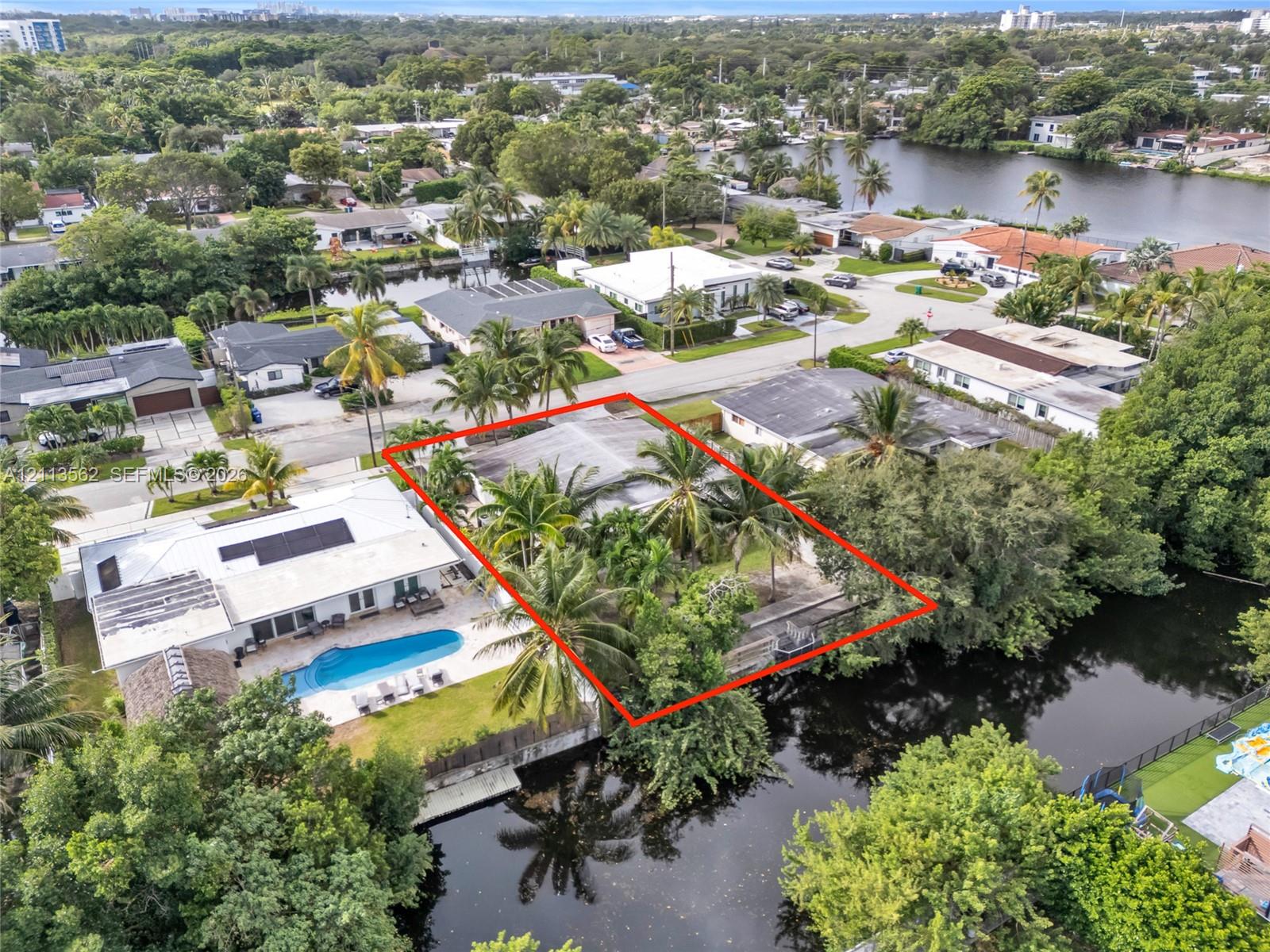 Aerial view of a waterfront property featuring a multi-pitched roofline, extensive mature palm landscaping, and direct water frontage along a canal