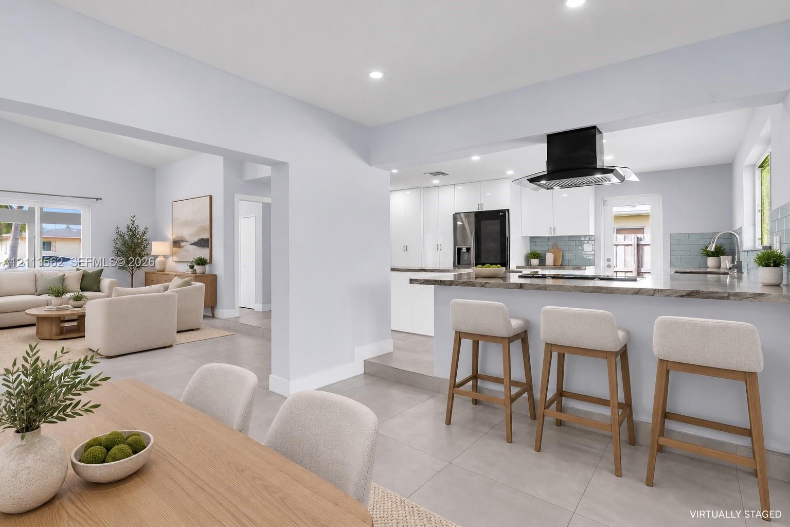 Kitchen featuring white cabinetry, stone-finish countertops, tile backsplash, and a black range hood, with large-format tile flooring throughout