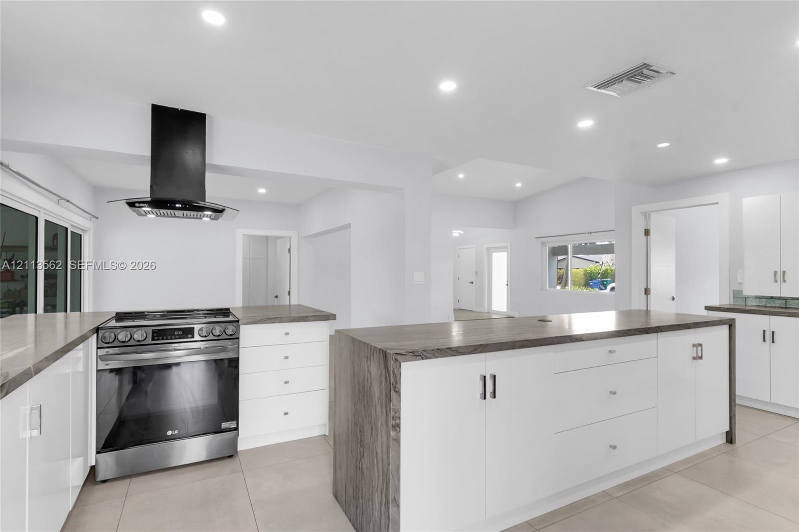 Kitchen featuring white flat-panel cabinetry, a central island with countertop seating, stone-finish countertops, stainless steel range, and a wall-mounted chimney-style range hood