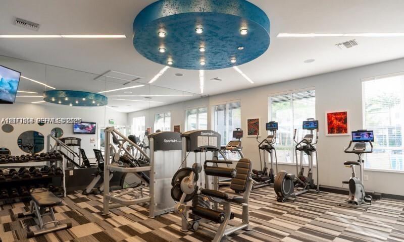 Fitness center featuring custom circular recessed ceiling lighting, wall-to-wall mirrors, patterned commercial carpeting, and large windows